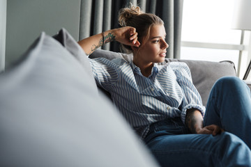 Fototapeta premium Image of serious caucasian woman looking aside while sitting on sofa