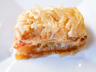 Delicious Greek sweet pastry named Galaktoboureko, made of semolina custard in filo, served with honey in white plate.