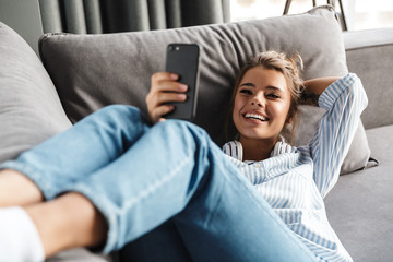 Image of smiling nice woman using cellphone while lying on sofa - Powered by Adobe