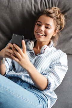 Image of smiling nice woman using cellphone while lying on sofa