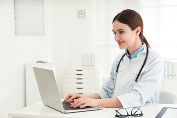 Young female doctor working with laptop at table in office