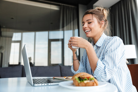Image of joyful nice woman drinking coffee and using laptop