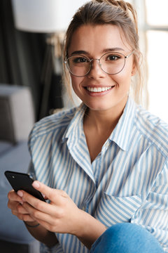 Image of happy young woman in eyeglasses smiling and using cellphone