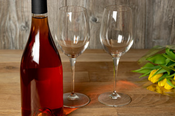 Bouquet of yellow tulips, a bottle of wine and two glasses on a wooden table. Holiday concept.