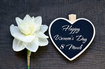 Happy Women's Day 8 March greeting card.Decorative heart with text and white spring Narcissus or Daffodil flower on a wooden background. Selective focus.