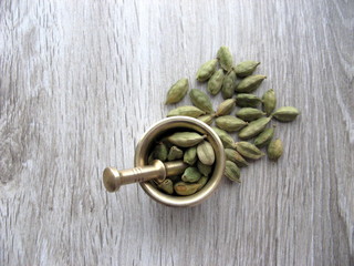 Green cardamom pods in brass mortar on wooden background. Top view. Close up.