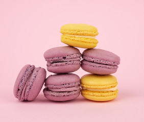 many multi-colored round baked macarons cakes on a light pink background