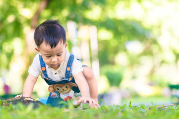 Happy little boy playin on green grass in city public park under tree sun light