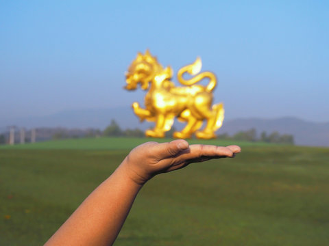 Woman tourist hand over blurry Large golden Singha (Lion) statue at sunrise sky background
