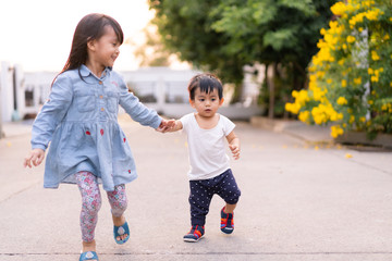 Adorable asian little toddler boy is holding hand with his big sister while he try to practice for...