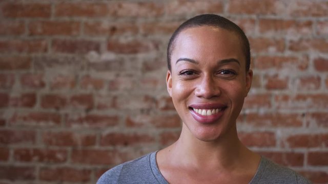 Head and shoulders portrait of smiling African American woman standing against brick wall in coffee shop - shot in slow motion