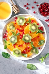 Fruits salad: kiwi, orange, pomegranate and mint served with honey. Healthy eating. Top view with copy space.