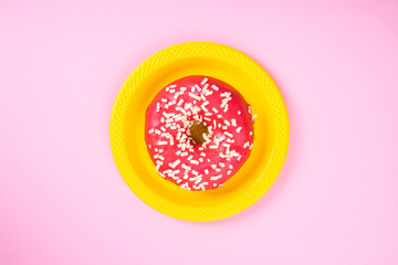 Pink donut on a yellow plate on a pink background. Sugar and obesity. Abstraction and minimalism.