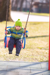 Happy little baby boy swinging on a swing on the playground