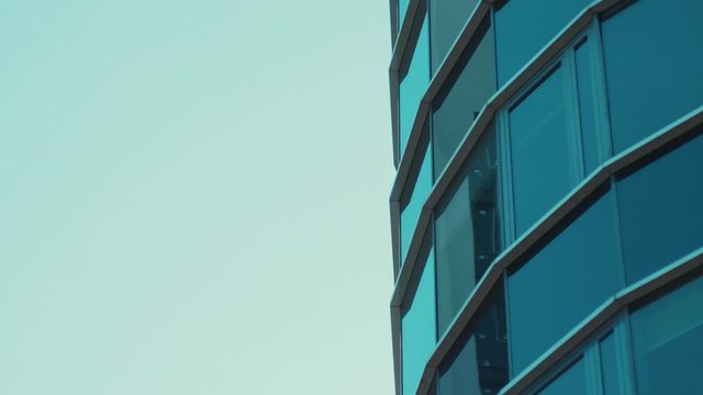 Blye glass transparent skyscraper from perspective angle view. Close-up of modern high office building against blue clear sky.