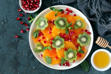 Fruits salad: orange, kiwi, pomegranate and mint served with honey. Top view with copy space. Healthy eating.