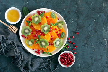 Fruits salad: orange, kiwi, pomegranate and mint served with honey. Top view with copy space. Healthy eating.