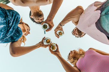 Group of happy friends drinking and toasting beer outdoors at the beach - Friendship concept with...