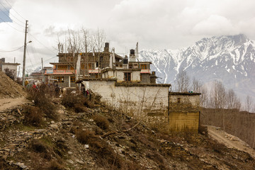Old traditional wood and stone buildings against a backdrop of snow covered Himalayan mountains in...