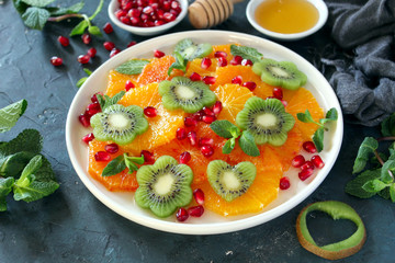 Fruits salad: orange, kiwi, pomegranate and mint served with honey. Top view with copy space. Healthy eating.