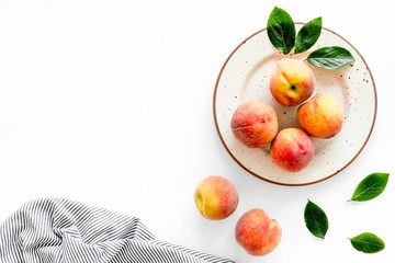 Summer lunch. Red peaches on white background with tablecloth and leaves top-down copy space