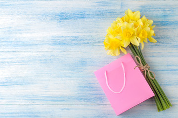 Spring flowers, yellow daffodils and gift bag on a blue wooden background. place for text