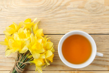 Spring flowers, yellow daffodils and a cup of tea on a natural wooden background. place for text