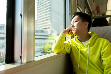 Sad young asian man looking through the window in the train carriage.