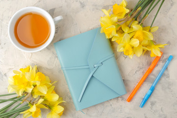 Spring flowers, yellow daffodils and a cup of tea, a notebook on a light concrete background. top view