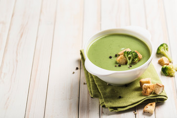 Cream broccoli soup with croutons in a white plate on a green napkin on a light wooden background. Concept of healthy nutrition.