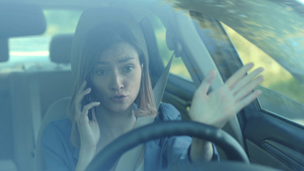 Angry young woman driver talking by phone while driving a car serious sunset sunlight communication...