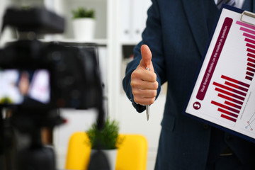Male in suit and tie show confirm sign arm making promo videoblog or photo session in office camcorder to tripod closeup. Vlogger promotion selfie solution or finance advisor management information © H_Ko