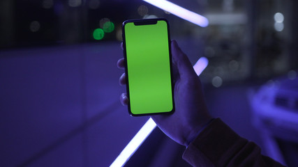 NEW YORK - April 19, 2019: Close up young man hands holding use smartphone with vertical green screen on night city colorful background white car communication device hands digital gadget phone