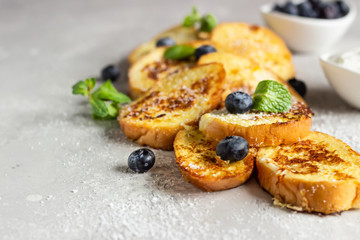 Torrijas, typical Spanish sweet fried toasts with blueberries, coconut flakes and mint on a light grey stone background. Traditional dessert for Lent and Easter.