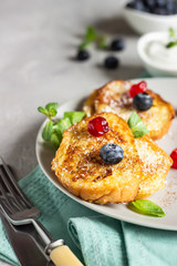 Delicious French toasts with blueberries, dried cherries and mint, light grey background. Sweet breakfast. 
