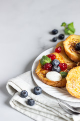 Delicious French toasts with blueberries, dried cherries and mint, light grey background. Sweet breakfast. 