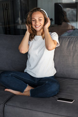 Image of smiling woman using wireless headphones while sitting on sofa