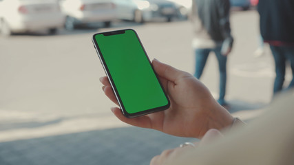 NEW YORK - May 19, 2019: Hands woman holding use vertical phone with green screen at sunny day typing scrolling pages swiping surfing internet technology smartphone chroma key message mobile phone