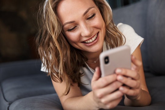 Image of smiling blonde woman using cellphone and wireless headphones