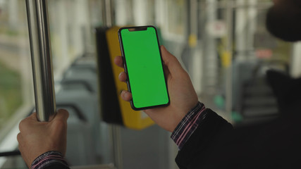 NEW YORK - May 19, 2019: Slow motion man young hand uses holding a mobile telephone with a vertical green screen background tram inside window key smartphone technology touch message display close up