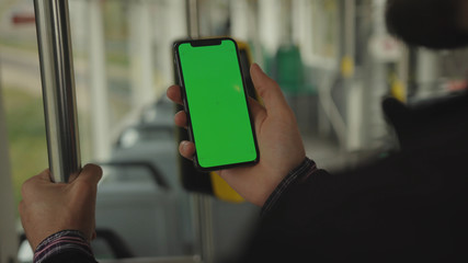 NEW YORK - May 19, 2019: Young man young hand uses holding a mobile telephone with a vertical green screen background tram seat people window key smartphone technology touch message display close up