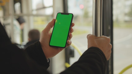 NEW YORK - May 19, 2019: Young man young hand uses holding a mobile telephone with a vertical green screen background tram seat people window key smartphone technology touch message display close up
