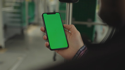 NEW YORK - May 19, 2019: Young man young hand uses holding a mobile telephone with a vertical green screen background tram chroma key smartphone technology touch message display close up
