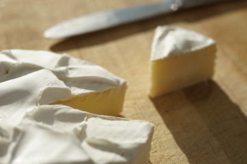 Camembert cheese with a triangular slice and a knife on a wooden board.