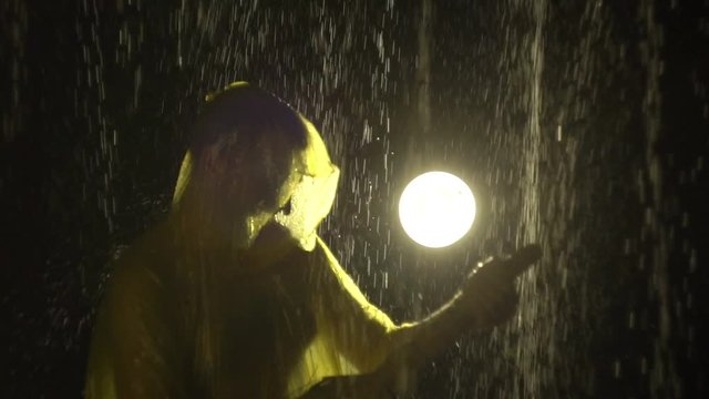 Man in raincoat with broom in his hands as if playing guitar in rain. One in yellow slicker with besom like a rock guitarist is fooling around and imagines that he is performs on stage during concert
