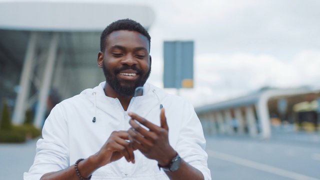 Smiling african american man uses futuristic glass phone walk at city look at camera smile nanosmartphone transparent electronic future global information innovation interface touch web slow motion