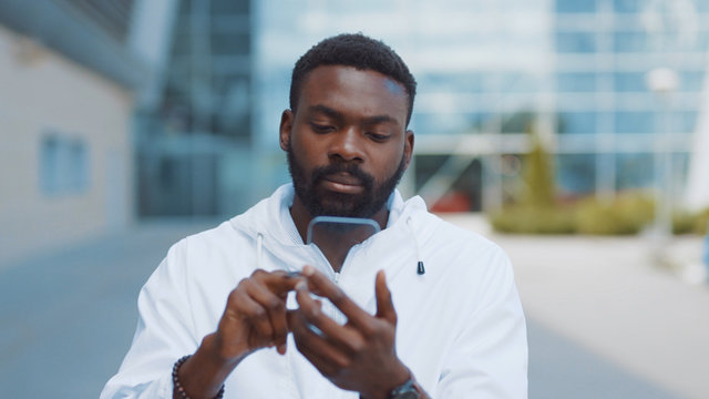 Smiling african american man uses futuristic glass phone walk at city look at camera smile nanosmartphone transparent electronic future global information innovation interface touch web slow motion
