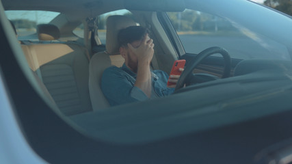 Young man driver beginner confused of failure first time driving in the car. Exhausted guy hitting steering wheel getting angry having problem.