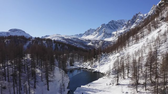 aerial over blue alpine lake revealing snowy mountain valley in sunny winter day.Europe Alps mountains outdoor establisher.4k drone forward flight establishing shot