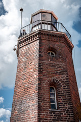 Fototapeta na wymiar An old red brick lighthouse in the background of cloudy blue sky in Ventes ragas, Lithuania
